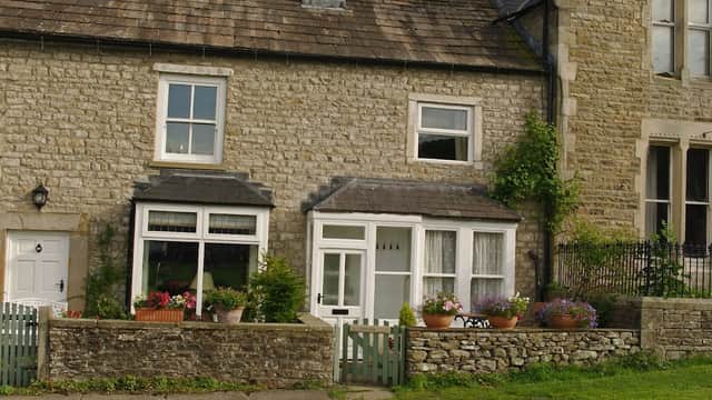 Stone cottage with flower-filled window boxes and a small garden, set in a rural Yorkshire landscape.
