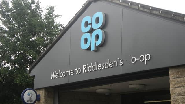 Co-op Food sign with "Welcome to Riddlesden's o-op" at a grocer's entrance, surrounded by greenery.