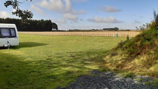 Expansive green field at McKies Caravan Park, with a caravan and wooden fence under a partly cloudy sky.