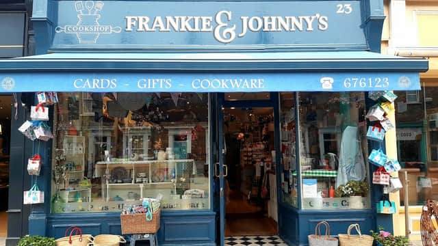 Quaint shopfront of Frankie & Johnny's Cookshop, featuring gifts, cards, and cookware, with colorful displays and baskets.