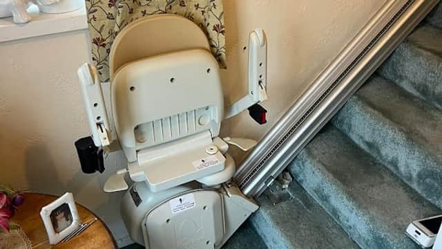 Stairlift installed at the bottom of a staircase, with a table and decorative curtains in the background.
