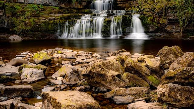 Serene waterfall cascading over rocks, surrounded by lush greenery in Cotterdale, Yorkshire.