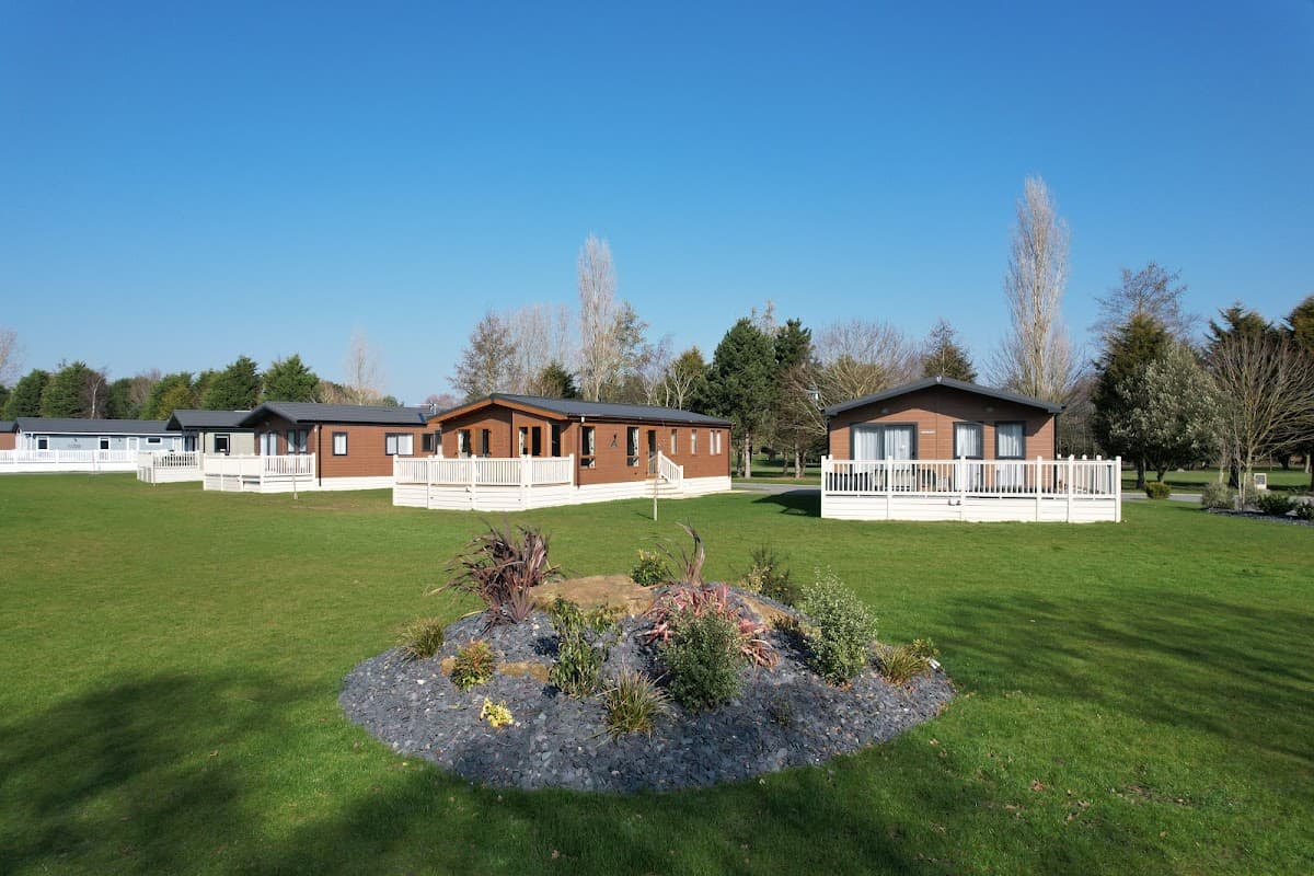 Lush green golf course with modern lodges and landscaped gardens under a clear blue sky.