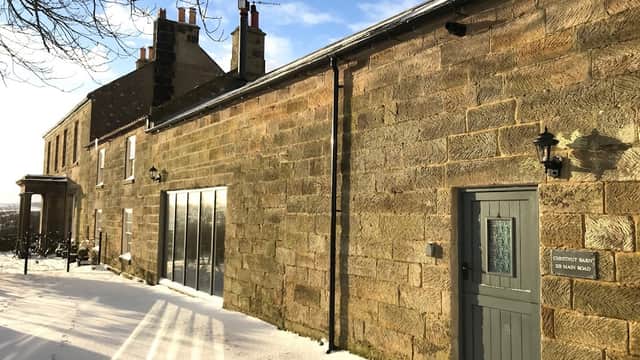 Chestnut Barn Holiday Cottage features a stone exterior, snow-covered ground, and large windows reflecting a sunny sky.