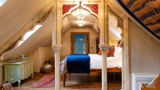 Stylish attic room with ornate arches, wooden flooring, a large bed, and decorative furnishings in a cozy ambiance.