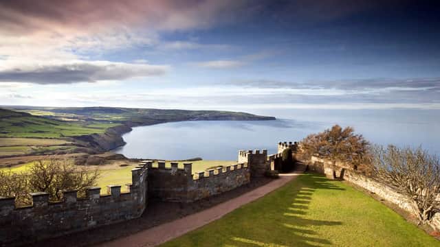 Stone battlements overlooking a green cliffside and expansive sea under a cloudy sky.