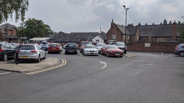 Pay & Display parking lot with various parked cars and buildings in the background under a cloudy sky.