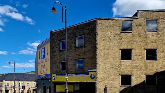 Multistory car park with yellow signage, stone walls, street lamps, and a person walking nearby under a blue sky.