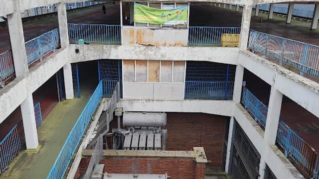 Abandoned multi-level car park with blue railings, a control tower, and overgrown plants in Bradford, Yorkshire.