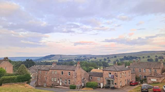Arkleside Country Guest House with stone facade, surrounded by green hills and a cloudy sky in Reeth, Yorkshire.