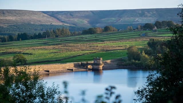 Scenic view of Digley Reservoir with green hills and trees, reflecting calm water under a clear blue sky.