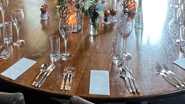 Elegant dining table set with floral arrangements, glassware, and candles, surrounded by cozy seating in a warm venue.