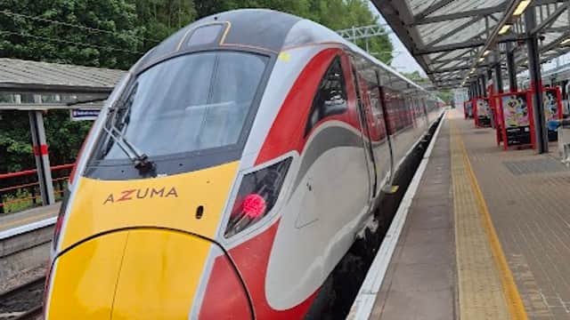 A sleek Azuma train at Bradford Forster Square Station, with green trees in the background and a covered platform.