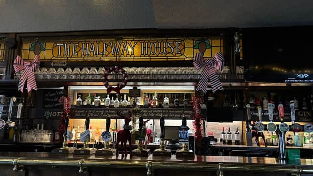 The Halfway House bar features a stained glass sign, festive decorations, and a variety of alcohol bottles on display.