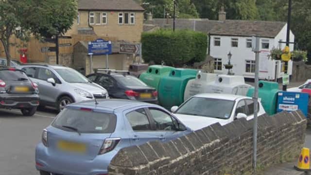 Honley Westgate Car Park with parked cars, stone wall, and nearby buildings under a cloudy sky.