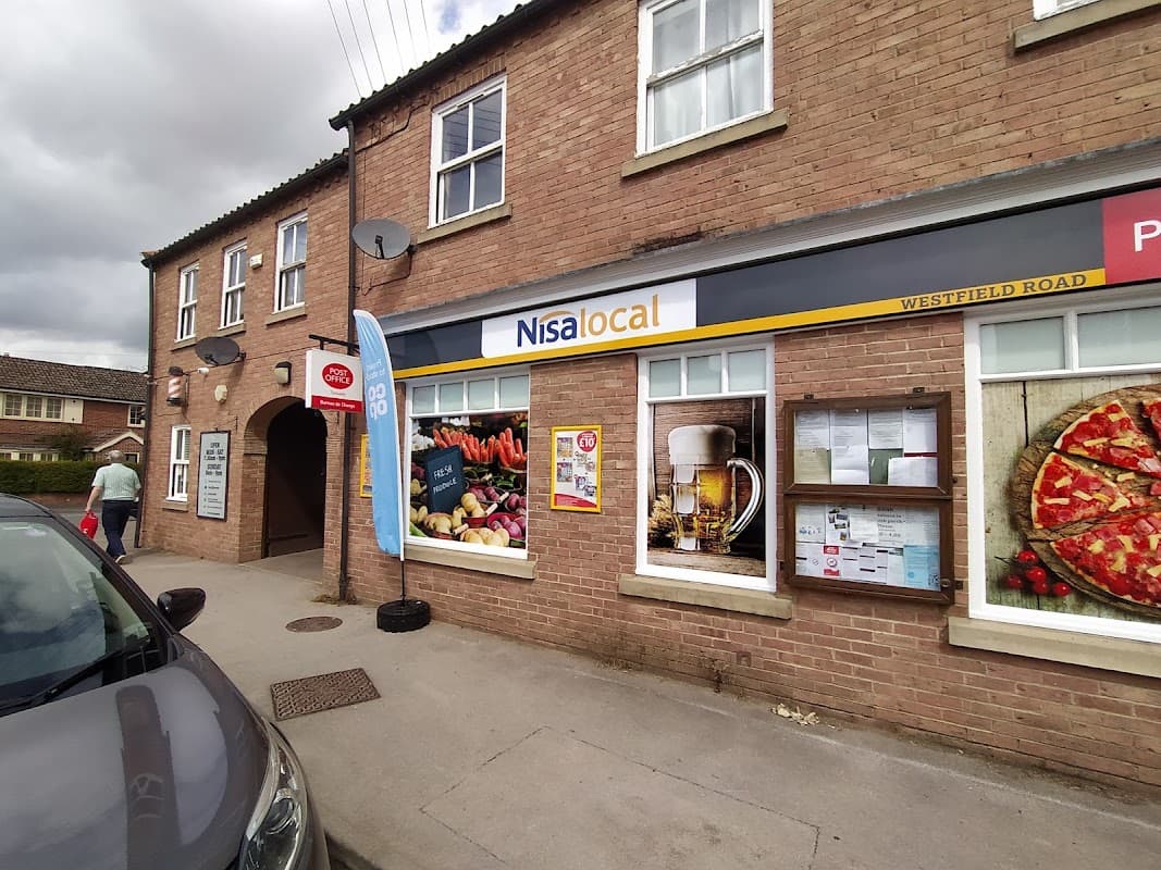 Nisa Local store exterior with a blue banner, posters of food and drinks, and a parked car on a street in Tockwith.
