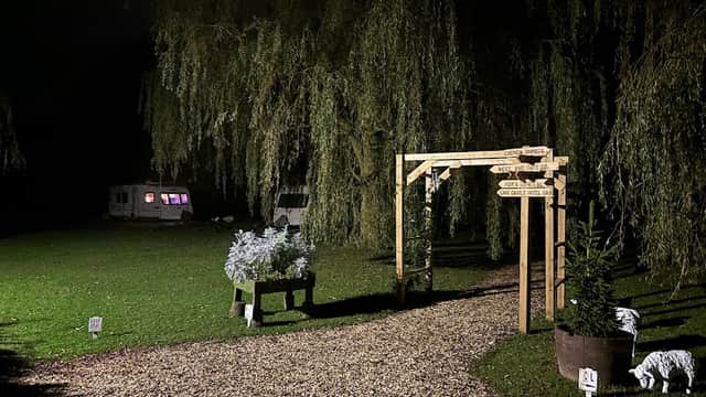 Wooden signpost at night directing to various areas, surrounded by greenery and caravans in a tranquil setting.