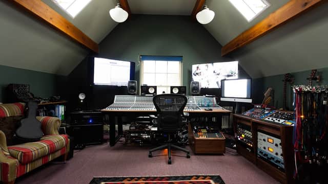 A cozy recording studio with large monitors, a mixing console, and various musical instruments on display.