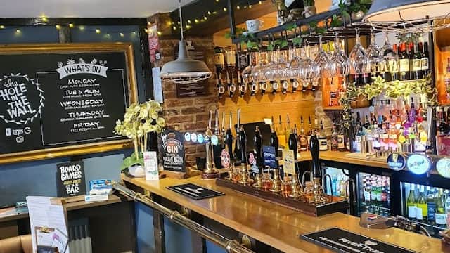 Cozy pub interior with a wooden bar, colorful drink displays, and a chalkboard menu in a warm, inviting atmosphere.