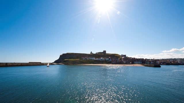 Bright sun over Whitby, with a view of the coastline and historic buildings along the water.