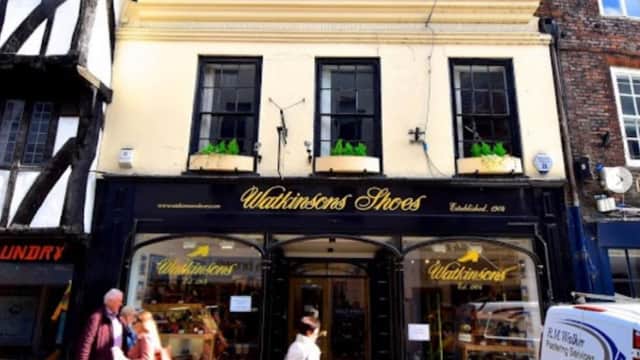 Historic shoe shop with a black storefront, yellow accents, and large windows displaying shoes in York, Yorkshire.