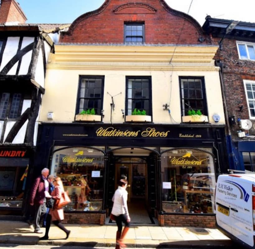 Historic shoe shop with a black storefront, yellow accents, and large windows displaying shoes in York, Yorkshire.