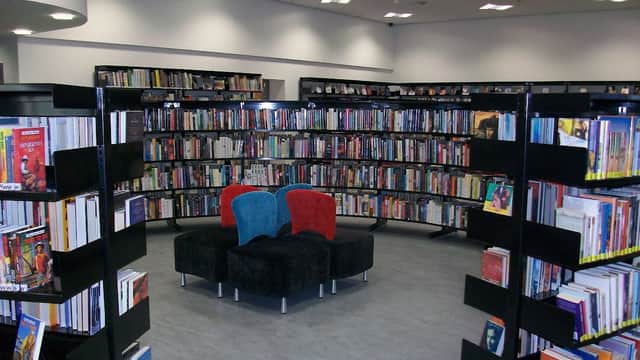 Bookshelves filled with books surround a cozy seating area with blue and red chairs in a modern library interior.