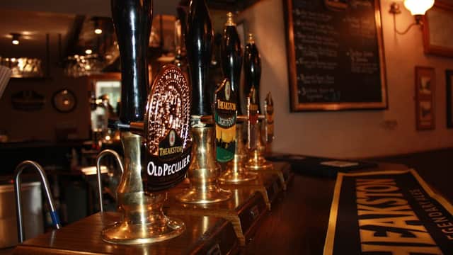 Four beer taps with distinctive labels, a wooden bar surface, and a chalkboard menu in a cozy pub setting.