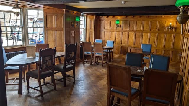 Wooden-paneled bar interior with tables and chairs, green lamps, and a herringbone floor in a cozy atmosphere.