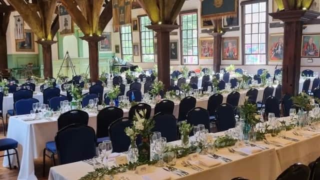 Elegant dining setup with white tablecloths, blue chairs, and floral centerpieces in a rustic hall with wooden beams.