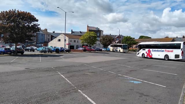 Car and coach park in Scarborough with several parked cars, a bus, and buildings in the background under a cloudy sky.