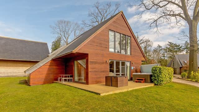 Modern wooden cabin with large windows, deck, and green lawn, surrounded by trees at Kilnwick Percy Resort.