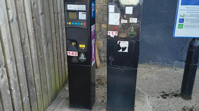 Two parking payment machines next to a wooden fence, with a parking sign visible in the background.