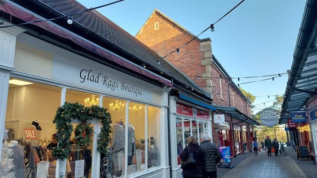 Charming shopping arcade with boutique storefronts, festive decorations, and string lights under a clear blue sky.