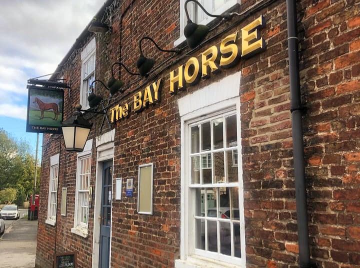 The Bay Horse pub features a brick facade, large windows, and a sign with a horse logo in Cherry Burton, Yorkshire.