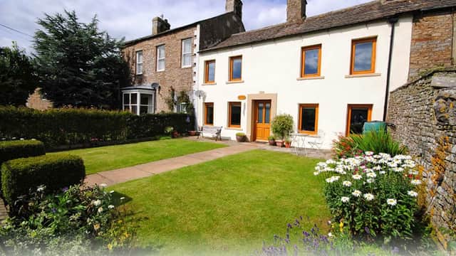 Charming holiday cottage with a well-kept garden, stone walls, and bright orange window frames in Sedbusk, Yorkshire.