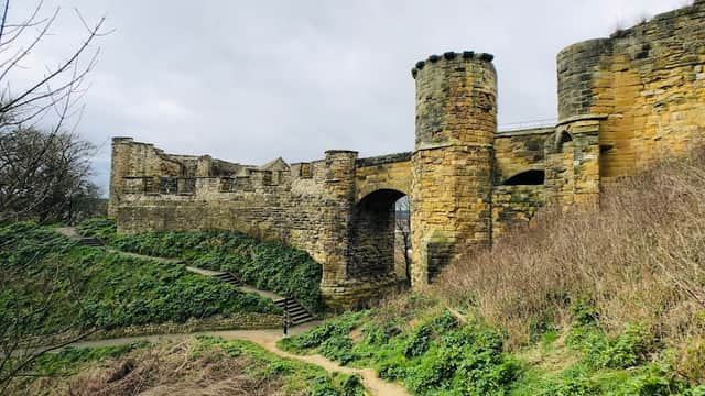 Stone castle ruins with towers, surrounded by greenery and a winding path in a cloudy sky.