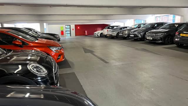 Parking garage with several parked cars, clear directional arrow, and a red wall in the background.