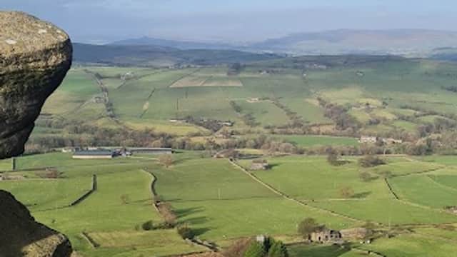 Expansive green hills and fields under a blue sky with scattered clouds, framed by rocky outcrops in the foreground.