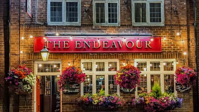 The Endeavour bar features a brick facade, vibrant flower baskets, and illuminated signage in Whitby, Yorkshire.