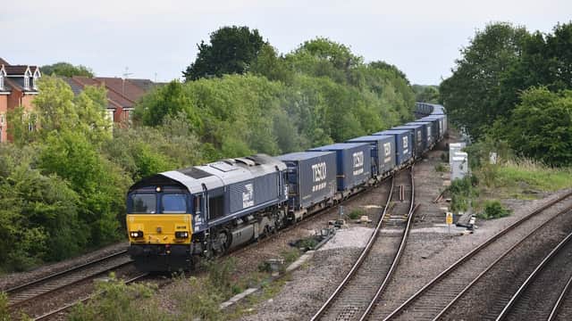 A freight train with blue containers passes through Church Fenton Station, surrounded by greenery and railway tracks.