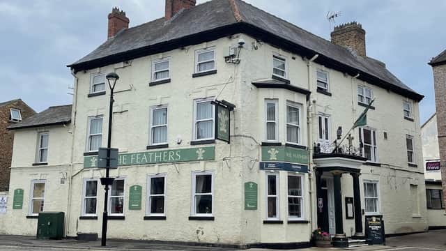 Historic building with a green sign reading "The Feathers," featuring a traditional facade and street lamps in Kilnwick Percy.