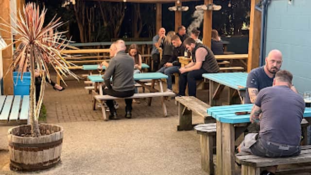 Outdoor seating area at The Queen Hotel, featuring wooden tables, patrons socializing, and greenery in Mosborough, Yorkshire.