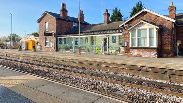 Garforth station building with brick faΓ§ade, green signage, and platforms beside railway tracks under a clear blue sky.