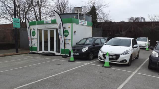 "We Buy Any Car" office with flags, parked cars, and green cones in a lot in Bessingby, Yorkshire.