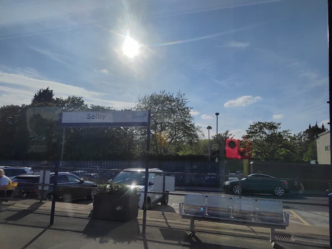 Pay & Display car park at Selby Station, with bright sun, blue sky, and parked cars visible.