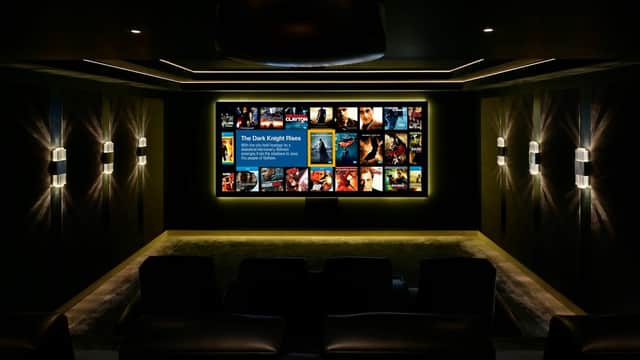 A modern home theater with a large screen displaying movie posters, dark walls, and plush seating.