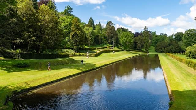 Lush green park with manicured lawns, trees, and a serene waterway under a bright blue sky.