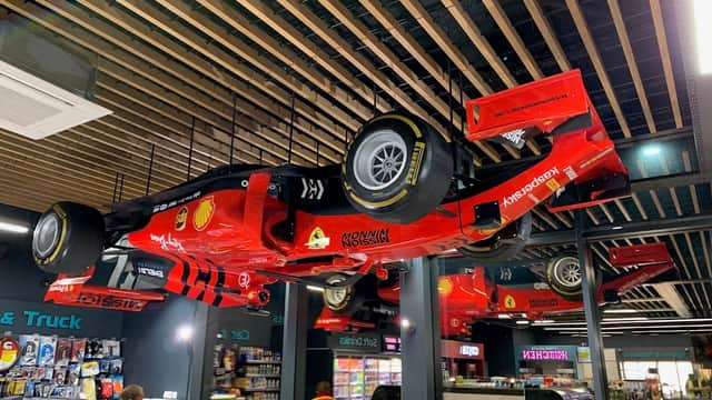 Ceiling-mounted red race cars with Shell logos, surrounded by shelves of snacks and drinks in a shop interior.
