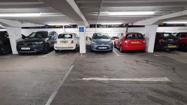 Multi-storey car park with parked vehicles, including grey, white, blue, and red cars in a well-lit underground setting.